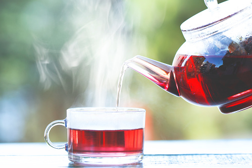Healthy herbal tea is poured from the kettle into a glass cup