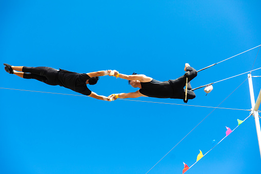 Two trapeze artists flying together in the sky