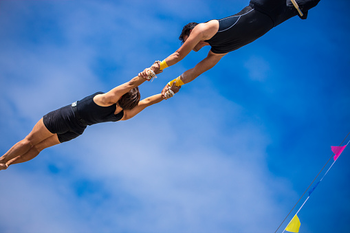 Two trapeze artists flying together in the sky