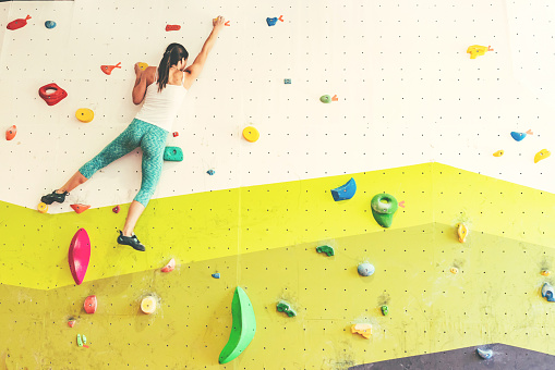 Beautiful young athletic woman climbing on an indoor climbing wall.