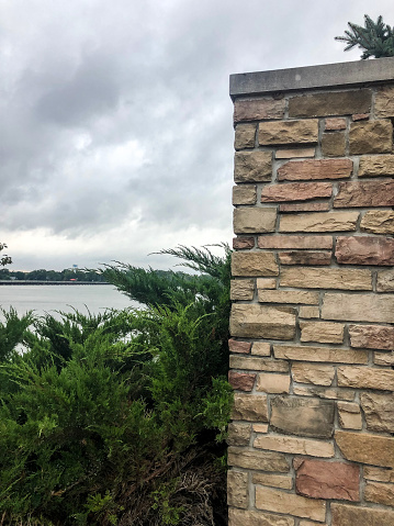 This background of brick wall by green bushes overlooking lake with clouds in sky would be perfect for your next project.