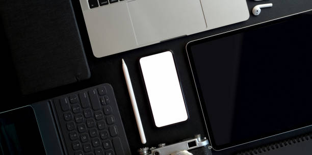 istock Top view of dark trendy workspace with blank screen smartphone and other electronics with office supplies 1179480766