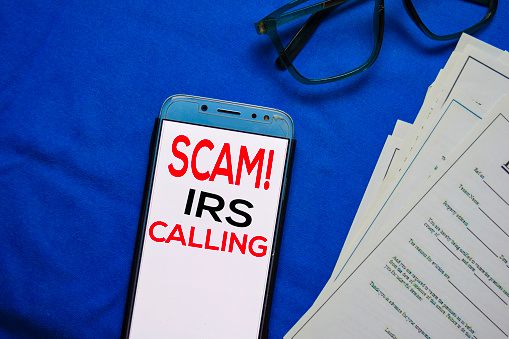 SCAM! IRS Calling text on Smart Phone isolated on office desk.
