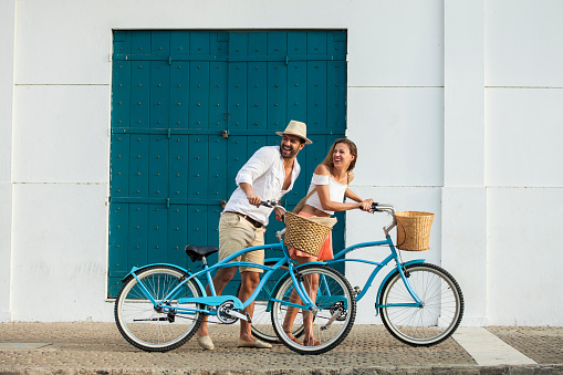 Latin ethnicity couple ages 25-35 are riding bicycles through the streets of Cartagena de Indias