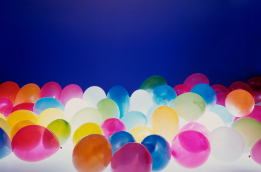 Lots of colorful balloons against blue background with light from bottom.