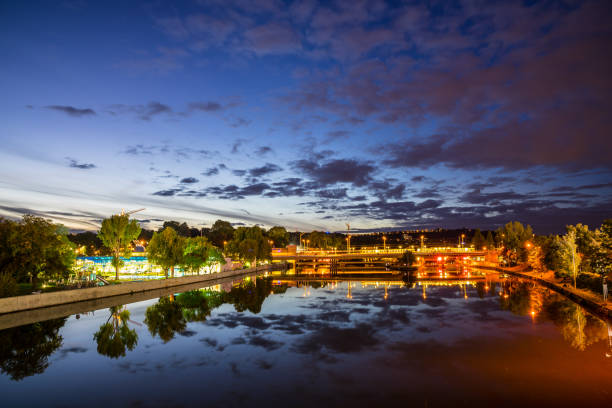 Germany, Scenic view over glassy neckar river reflecting tram and train driving by swimming pool of stuttgart bad canstatt by night in beautiful atmosphere