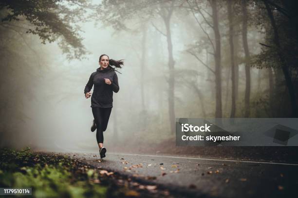 Young Athletic Woman Jogging On The Road In Foggy Forest Stock Photo - Download Image Now