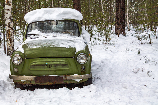 Retro green car stands in the winter forest. Old car under the snow