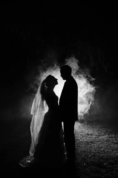 Photo of silhouette of a bride and groom at night with a smokey background