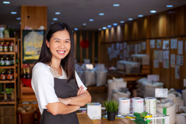 成熟した女性食料品店のオーナー、店内で腕を組んで立っている - supermarket sales clerk grocer apron ストックフォトと画像