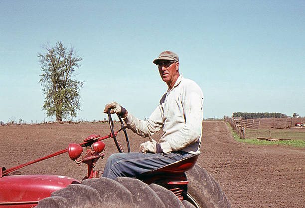 farmer on tractor 1964, retro Farmer on tractor during spring planting. Wellman, Iowa, USA 1964. Agfachrome scanned film with grain. farmer tractor iowa farm stock pictures, royalty-free photos & images