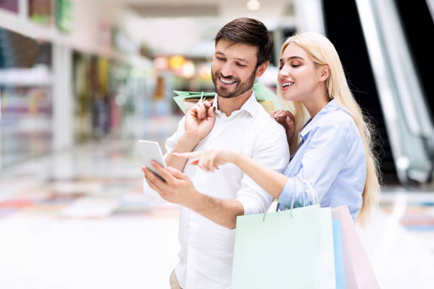 istock Smiling Couple Using Cellphone Searching Sales Offers Standing In Mall 1179525443