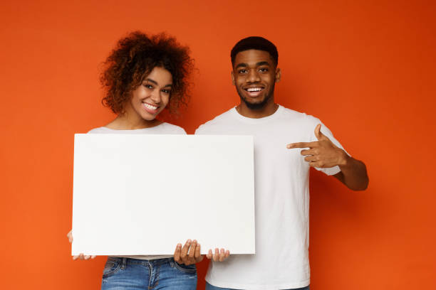 istock Positive black man and woman pointing at white empty board 1179526925