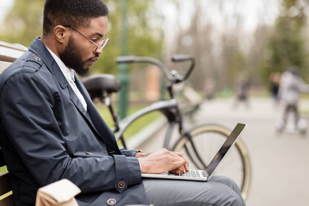 istock Afro businessman using laptop in park, sitting on bench 1179527391