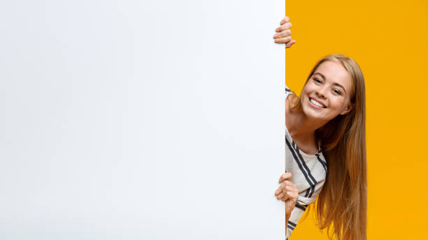 hermosa adolescente mirando fuera de la placa blanca en blanco - businesswoman advertise placard advertisement fotografías e imágenes de stock