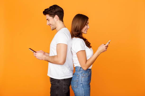 pareja joven usando teléfonos celulares, de pie de espaldas - couple dependency standing men fotografías e imágenes de stock