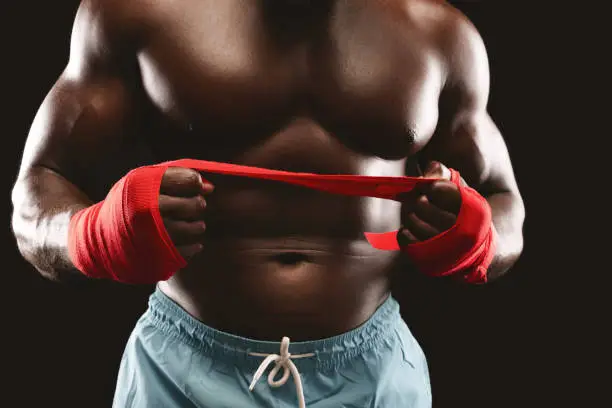 Photo of Professional boxer pulling red sports bandage over black background