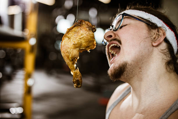 Nerdy male athlete craving for roasted chicken leg on a net in a gym.