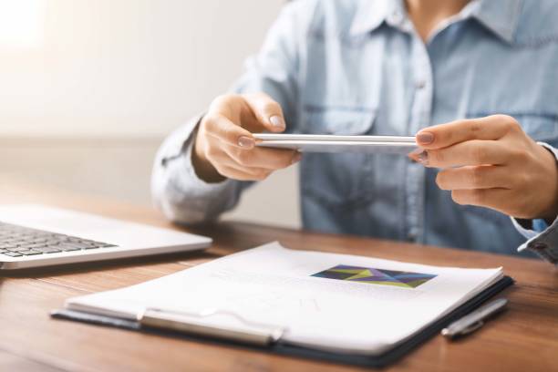 Woman using smartphone in horizontal orientation taking photo of documents