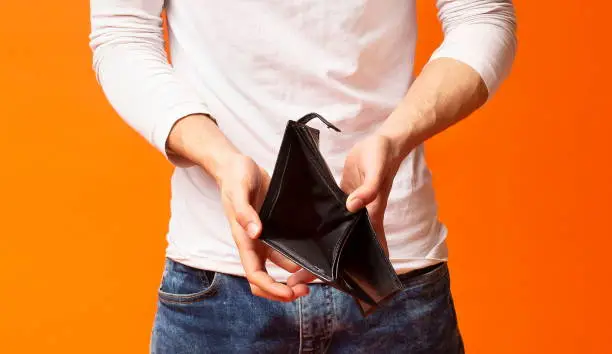 Poverty and absence of money. Empty wallet in hands of unemployed black man, orange studio background