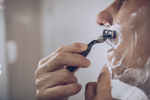 Adult man shave his beard in domestic bathroom