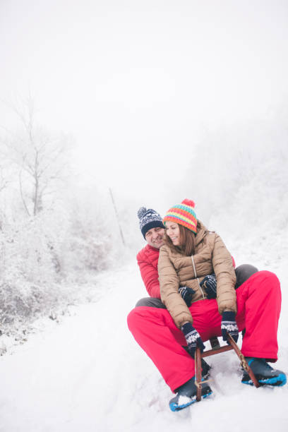 pares novos que sledding e que apreciam no dia de inverno - pair couple cheerful laughing - fotografias e filmes do acervo