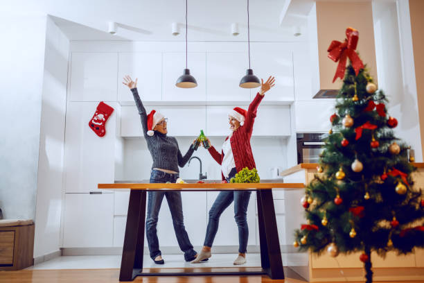 istock Happy senior woman toasting with beer with her daughter while standing in kitchen. Both having santa hats on heads. 1179552172