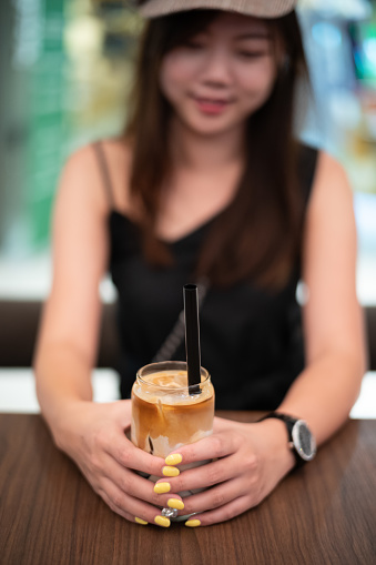 Female hand holding iced cafe latte on top of wooden table