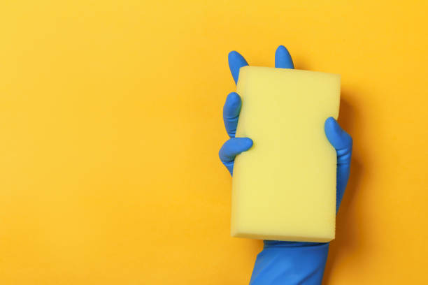 istock A hand in a protective blue glove holds a sponge on a yellow colored background 1179557346