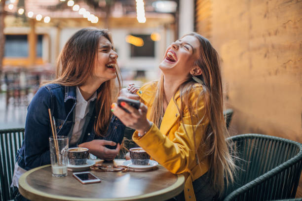 Two women, sitting outdoors in pub, two girlfriends using smart phone together.