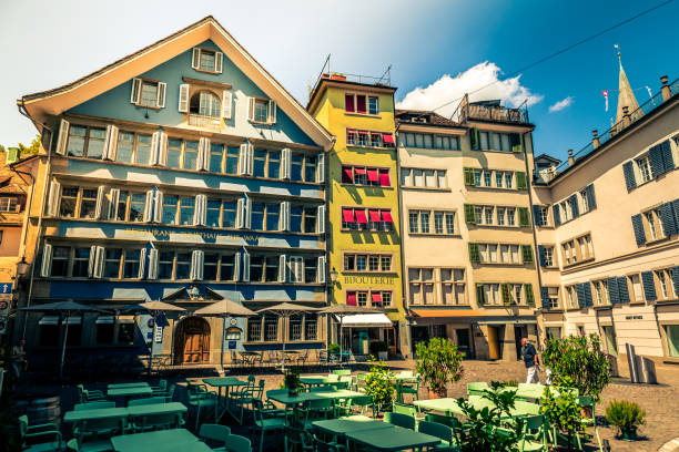 Zurich, Switzerland - 4 August, 2019: Color image depicting the beautiful traditional architecture of the old town of Zurich in Switzerland. Low angle image looking up at an ancient clock tower and an old building with balconies adorned with fresh flowers. Room for copy space.