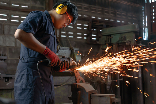 Engineer operating angle grinder hand tools in manufacturing factory - Mechanical engineering student using power tool with hot metal sparks wearing safety equipment - workshop and occupation concept