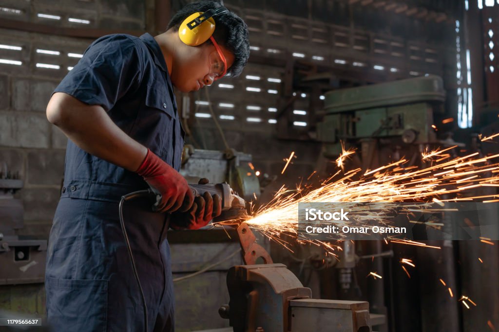 Asian Mechanical engineer operating power tools with metal sparks and copy space Engineer operating angle grinder hand tools in manufacturing factory - Mechanical engineering student using power tool with hot metal sparks wearing safety equipment - workshop and occupation concept Occupation Stock Photo