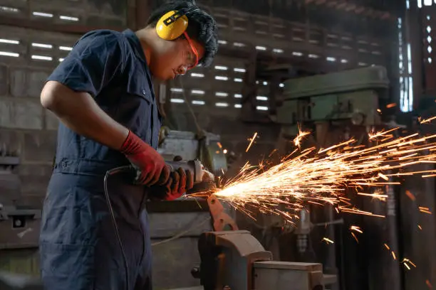 Photo of Asian Mechanical engineer operating power tools with metal sparks and copy space