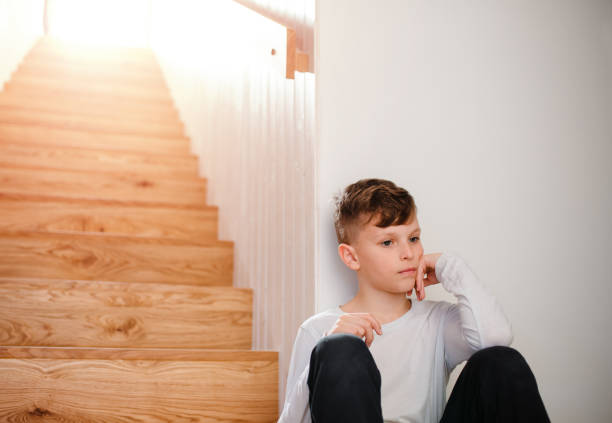 A sad small boy sitting on the floor by the stairs. Copy space.