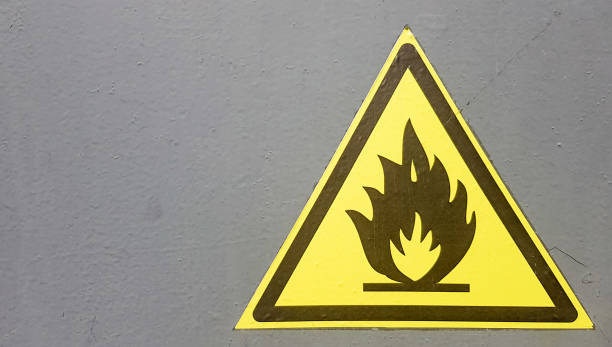 istock Fire warning icon, sign on a yellow label on a gray background. Flammable. Yellow triangle on a metal wall. Background with copy space 1179567497