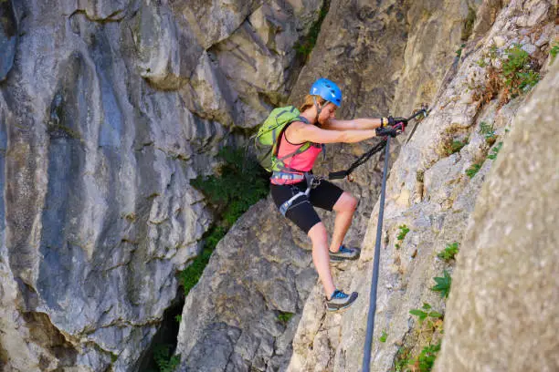 Photo of Tourist on via ferrata in Turda gorge (Cheile Turzii) Romania, crossing a traverse section, using straight arms and good climbing technique.