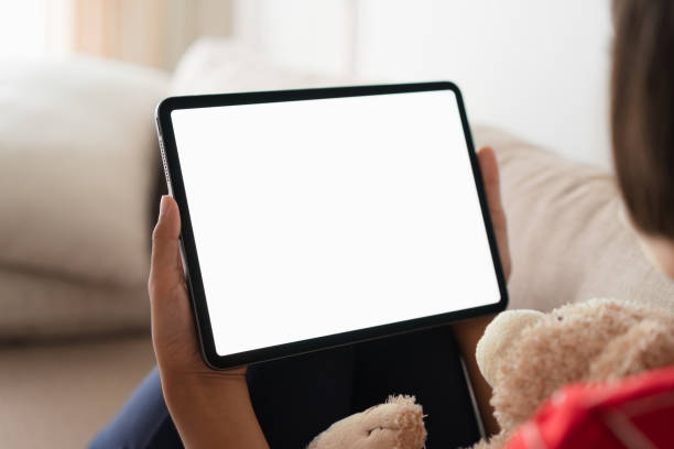 Mockup, Blank digital tablet in the hand of Asian  little girl, Tablet  white screen. While sitting on the sofa at her home. stock photo