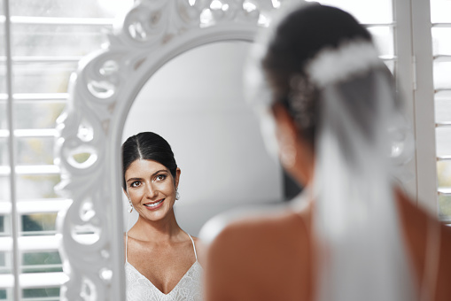 Rearview shot of an attractive young bride looking in the mirror while getting ready for her wedding ceremony