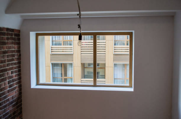 istock A new empty loft-style apartment, with a brick wall, white walls and a huge window through which you can see the modern new house opposite. One light bulb hangs from the ceiling. The concept of new housing, moving, housewarming 1179570284