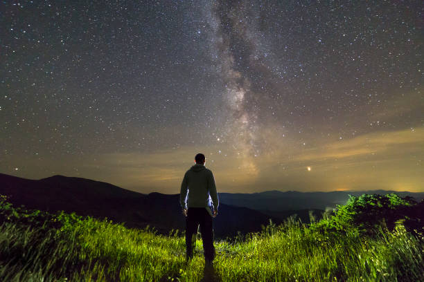 dark silhouette of a man standing in mountains at night enjoying milky way view. - milky way galaxy space star imagens e fotografias de stock