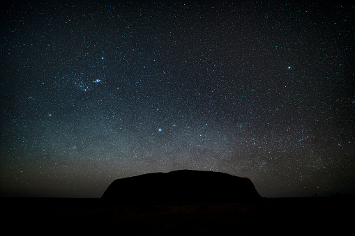 Northern Territory, Australia - August 08, 2019: Night-time in the heart of the Australian Outback, and countless stars overhead barely illuminate the massive form of Uluru that looms majestically on the horizon.