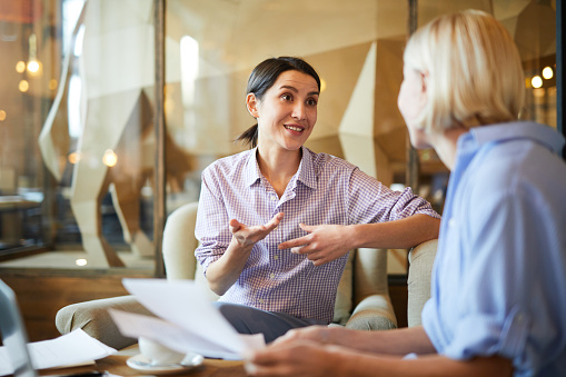 Warm toned portrait of contemporary businesswoman gesturing actively while talking to female colleague during business meeting in cafe, copy space