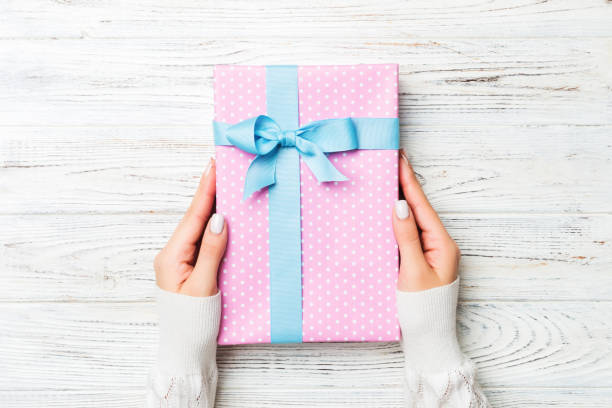istock Top view woman hands holding present box with colored bow on white rustic wooden background with copy space 1179574423