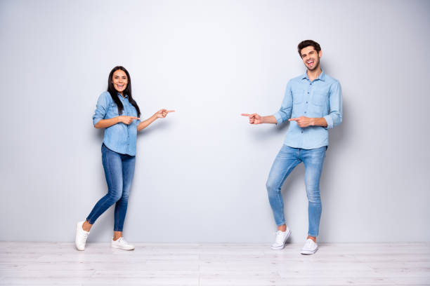 full length photo of guy and lady advising buy new product for low price indicating fingers empty space wear casual jeans clothes isolated grey color background - dirigindo imagens e fotografias de stock