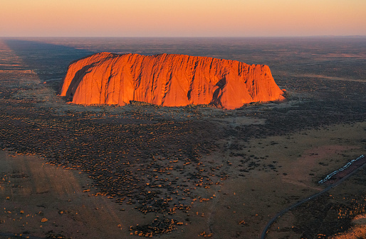 Northern Territory, Australia - August 08, 2019: Late afternoon sun shines down on the landscape around Uluru, in Australia's Northern Territory. A place sacred to the local Anangu people and adored by photographers, it's also a UNESCO World Heritage site. Elevated view from a helicopter.