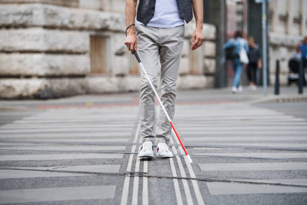 Midsection of young blind man with white cane walking across the street in city. Midsection of young unrecognizable blind man with white cane walking across the street in city. blind persons cane stock pictures, royalty-free photos & images