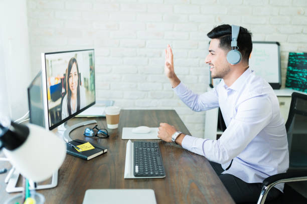 Professionals Greeting Through Conference Call Confident young salesman waving at colleague during video call on computer at desk audio equipment photos stock pictures, royalty-free photos & images