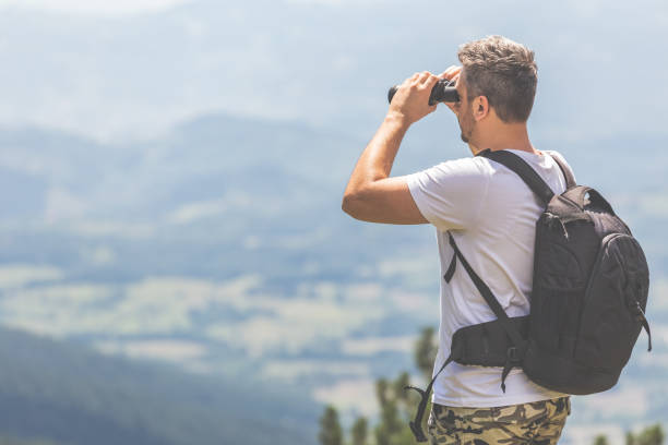 istock Traveler with backpack standing on the top of the mountain and using binoculars 1179586679