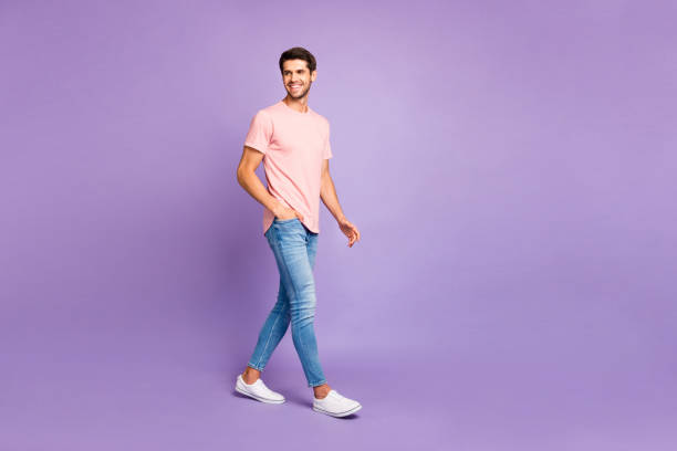 vue pleine longueur de taille de corps de son il il gentil le gai gai gai joyeux joyeux bon gars confiant utilisant le t-shirt rose se promenant d'isolement sur le fond de couleur pastel de lilas violet violet - t shirt white men jeans photos et images de collection